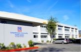 A two-story health center building with a blue and red sign reading "Comprehensive Community Health Centers," and several cars parked in front.